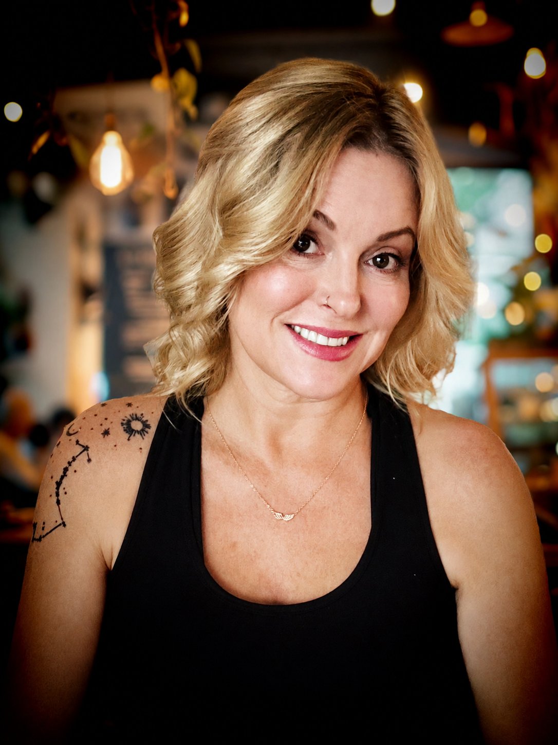 Melissa Leline, Licensed Massage Therapist, smiling in a warmly lit room, her constellation tattoo on her shoulder